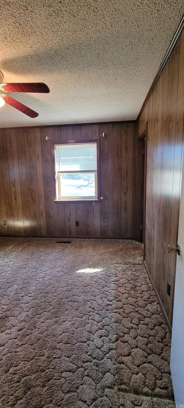 carpeted empty room featuring ceiling fan, a textured ceiling, and wooden walls