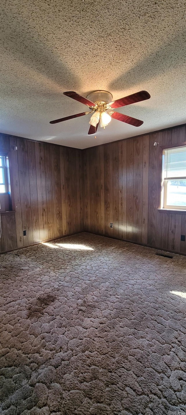 unfurnished room featuring carpet flooring, a textured ceiling, ceiling fan, and wood walls