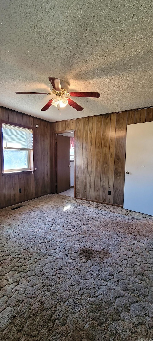 carpeted empty room featuring a textured ceiling and wooden walls