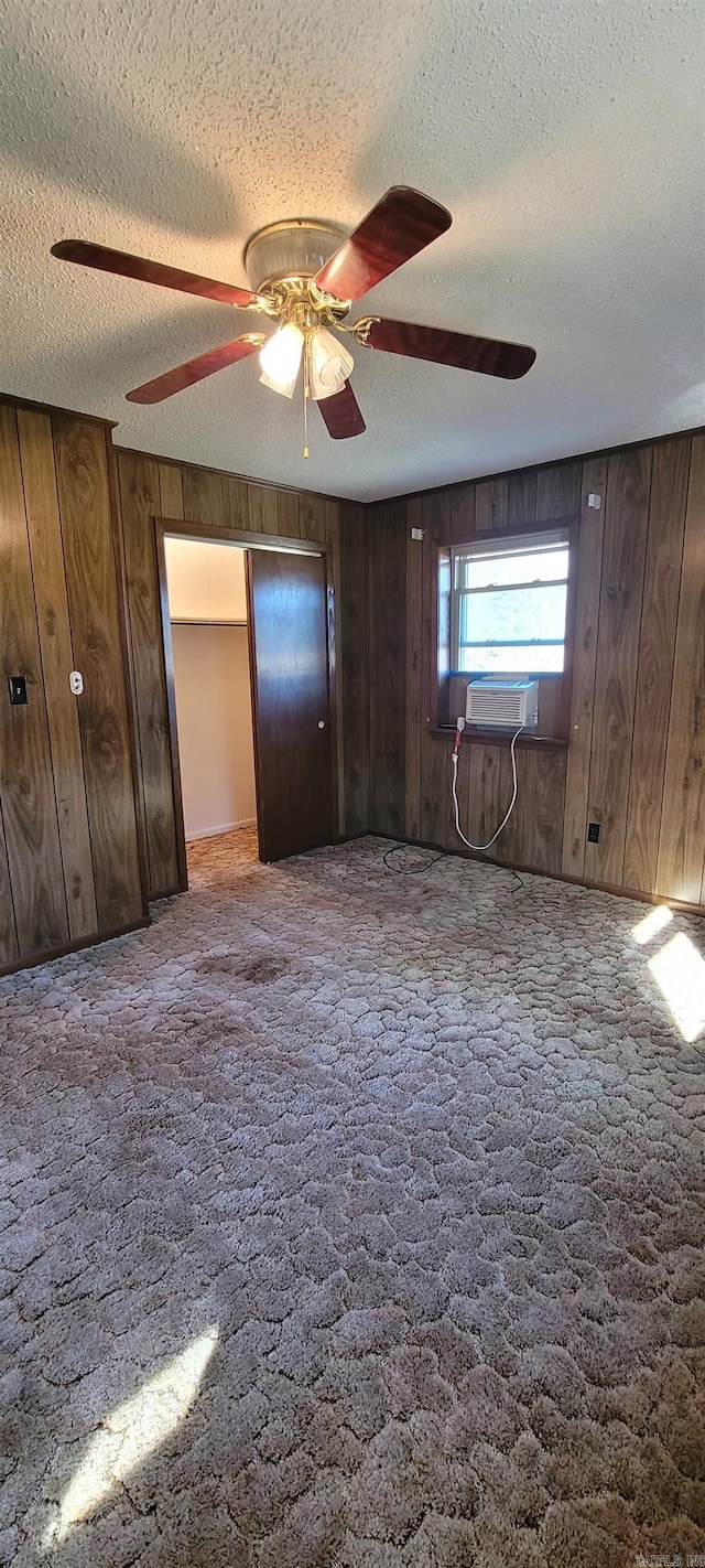 unfurnished bedroom with ceiling fan, wood walls, cooling unit, carpet floors, and a textured ceiling