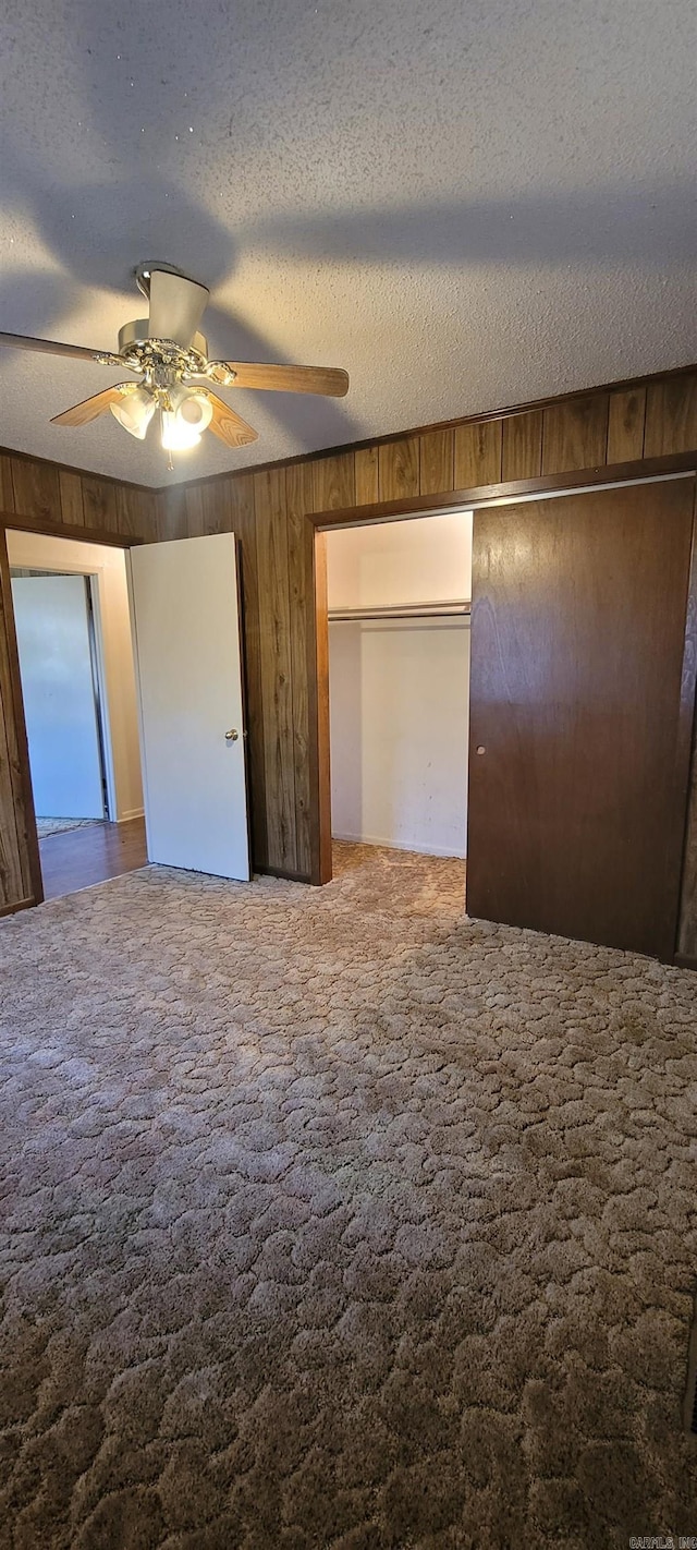 unfurnished bedroom with carpet flooring, ceiling fan, wood walls, and a textured ceiling