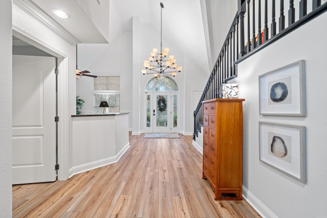 entryway with ceiling fan with notable chandelier, light wood-type flooring, high vaulted ceiling, and french doors