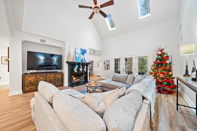 living room with a skylight, ceiling fan, high vaulted ceiling, and light wood-type flooring