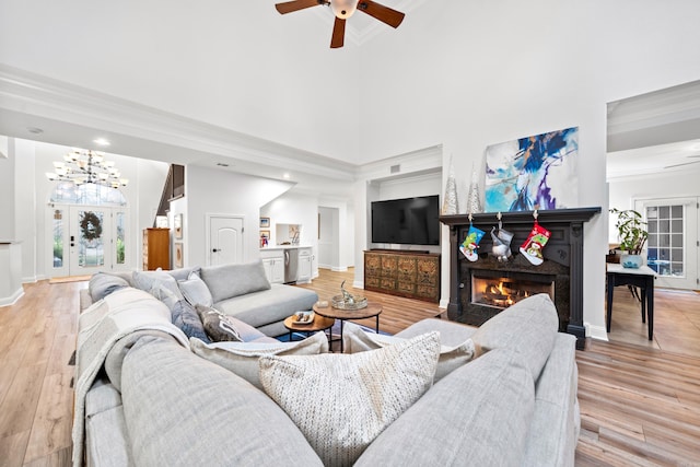 living room with ceiling fan with notable chandelier, a towering ceiling, light wood-type flooring, and crown molding