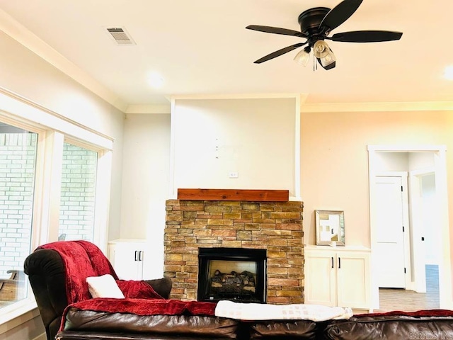 living room with a stone fireplace, ceiling fan, and crown molding