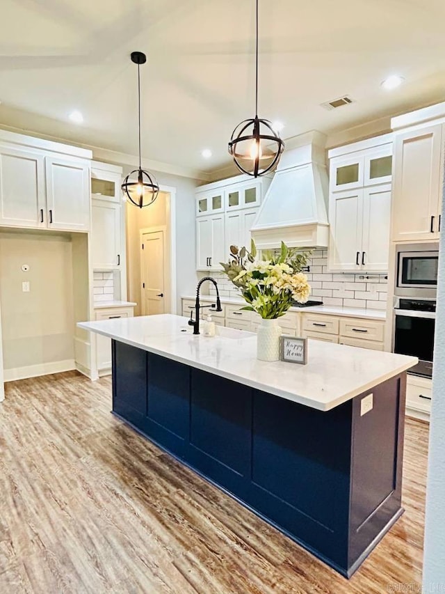 kitchen featuring backsplash, premium range hood, a kitchen island with sink, hanging light fixtures, and stainless steel appliances