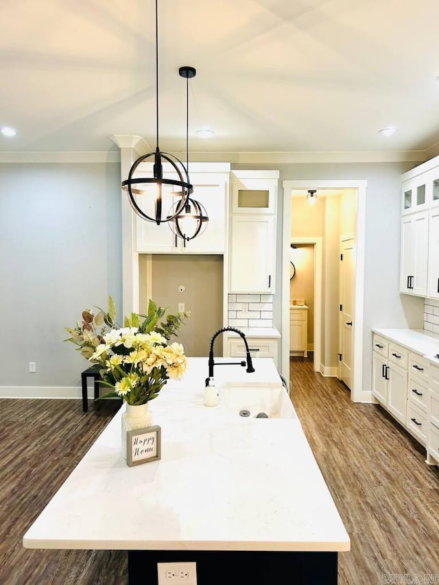 kitchen with backsplash, a kitchen island with sink, hanging light fixtures, and sink