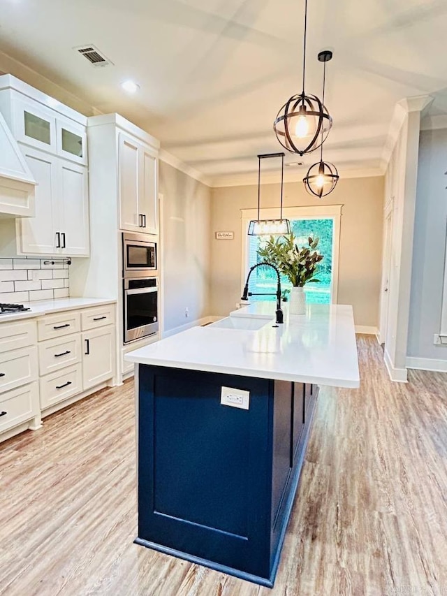 kitchen featuring a kitchen island with sink, sink, tasteful backsplash, white cabinetry, and stainless steel appliances