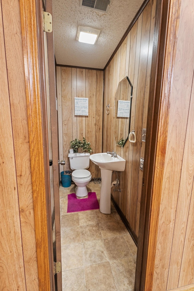 bathroom with wood walls, toilet, and a textured ceiling