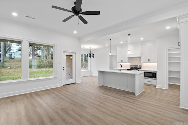 kitchen with a wealth of natural light, a kitchen island with sink, sink, and white cabinets