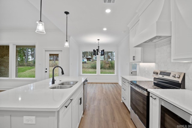 kitchen with custom range hood, stainless steel appliances, a kitchen island with sink, sink, and hanging light fixtures