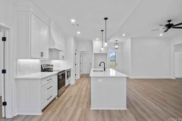 kitchen with light wood-type flooring, electric range, decorative light fixtures, a center island with sink, and white cabinetry