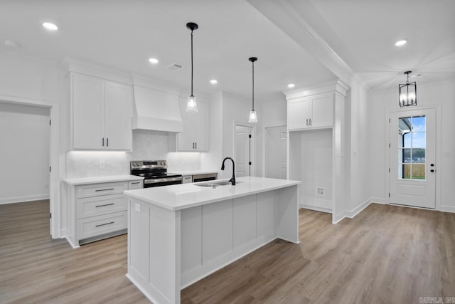 kitchen with sink, premium range hood, stainless steel range with electric stovetop, a center island with sink, and white cabinets