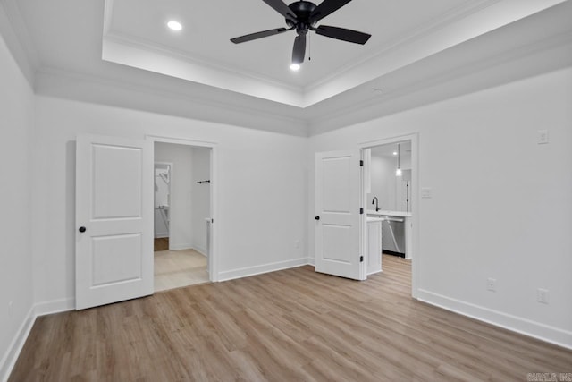 unfurnished bedroom with light wood-type flooring, a tray ceiling, ensuite bath, and crown molding