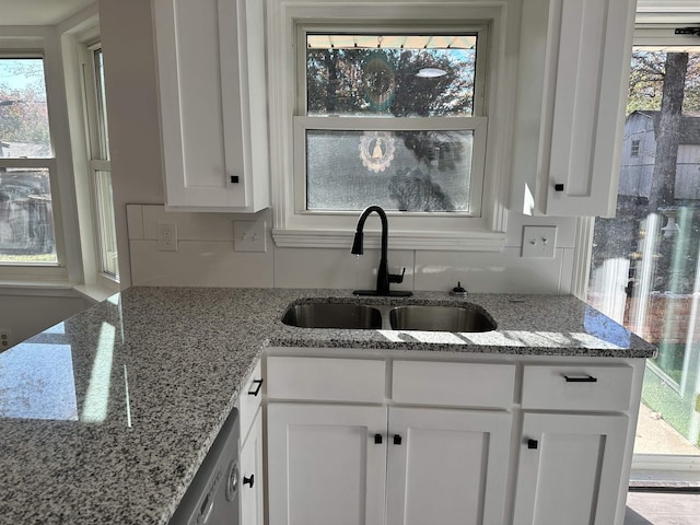 kitchen with dishwasher, light stone counters, white cabinetry, and sink