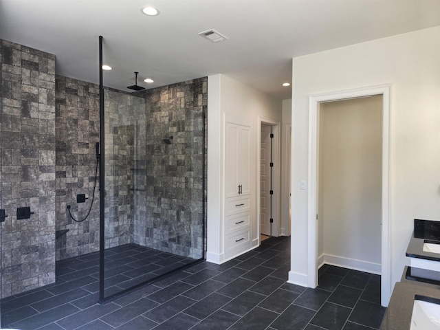 bathroom with a tile shower, tile patterned flooring, vanity, and tile walls