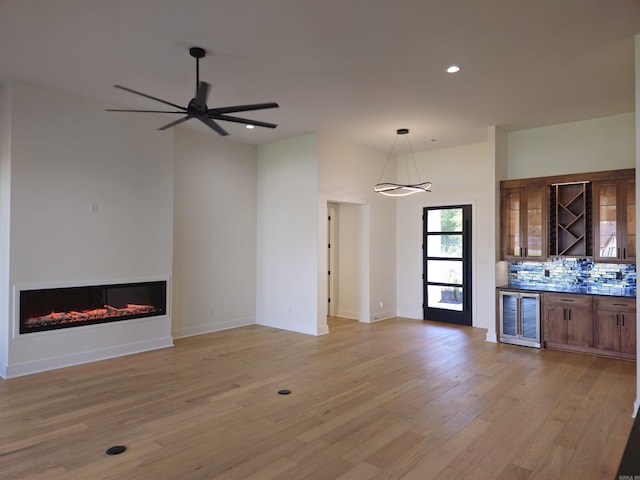 unfurnished living room with wine cooler, ceiling fan, and light wood-type flooring