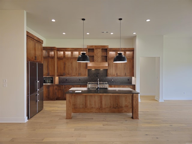 kitchen featuring hanging light fixtures, a kitchen bar, a kitchen island with sink, high end fridge, and light wood-type flooring