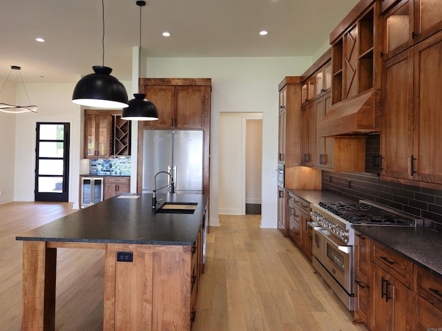 kitchen featuring backsplash, pendant lighting, light hardwood / wood-style flooring, high quality appliances, and an island with sink