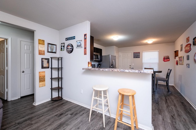 kitchen with kitchen peninsula, a kitchen breakfast bar, light stone countertops, appliances with stainless steel finishes, and dark hardwood / wood-style floors