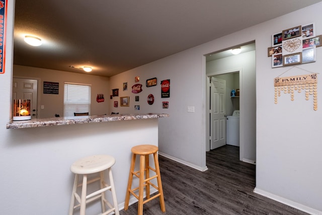 kitchen with light stone countertops, dark hardwood / wood-style floors, kitchen peninsula, washer / dryer, and a breakfast bar