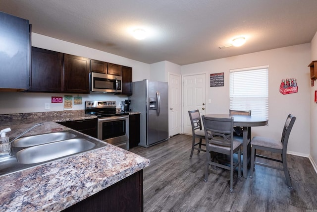 kitchen featuring dark brown cabinetry, sink, stainless steel appliances, dark hardwood / wood-style floors, and a textured ceiling