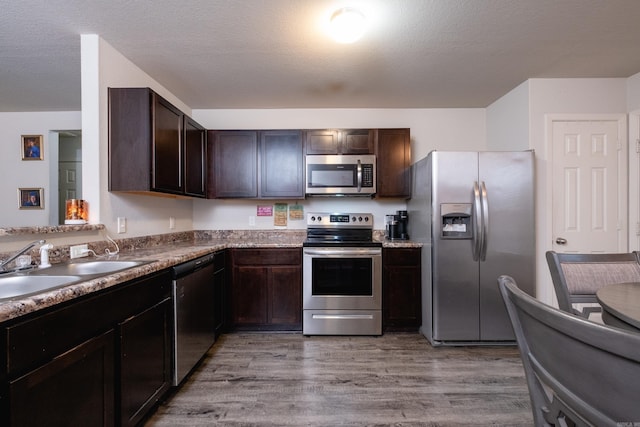 kitchen with sink, stainless steel appliances, light hardwood / wood-style flooring, a textured ceiling, and dark brown cabinets