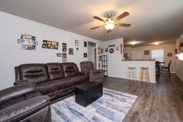 living room with a textured ceiling, ceiling fan, and dark wood-type flooring