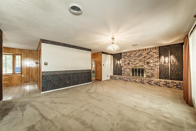 unfurnished living room featuring light carpet, a brick fireplace, a textured ceiling, wooden walls, and a chandelier