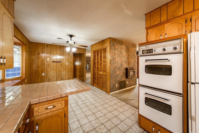 kitchen with a textured ceiling, tile countertops, wood walls, and white appliances