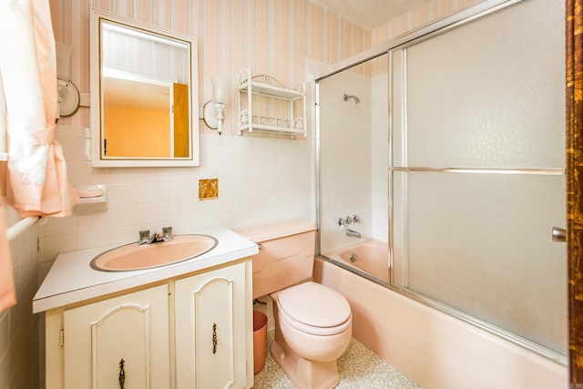 full bathroom featuring combined bath / shower with glass door, backsplash, vanity, tile walls, and toilet