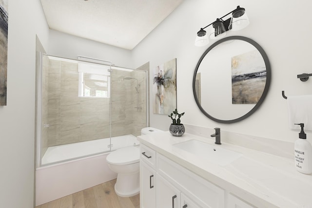 full bathroom featuring vanity, shower / bath combination with glass door, hardwood / wood-style flooring, toilet, and a textured ceiling