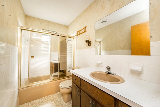 full bathroom featuring toilet, vanity, tile walls, and combined bath / shower with glass door