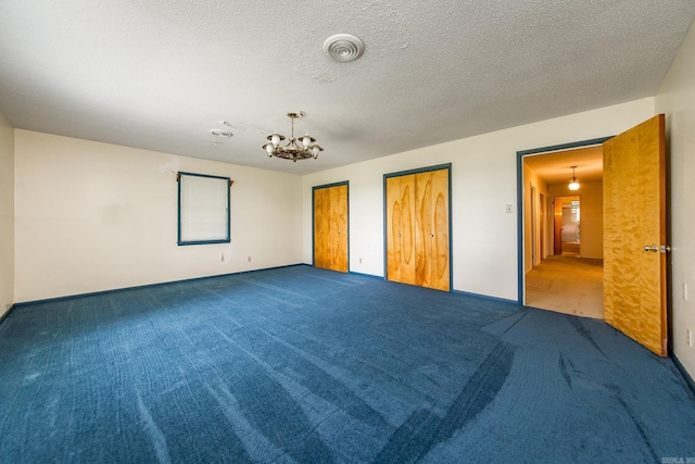 unfurnished bedroom featuring carpet, a textured ceiling, two closets, and an inviting chandelier