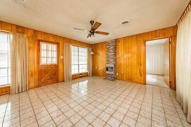 unfurnished living room with heating unit, ceiling fan, wooden walls, and a textured ceiling