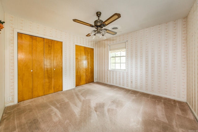 unfurnished bedroom featuring ceiling fan, carpet floors, and two closets