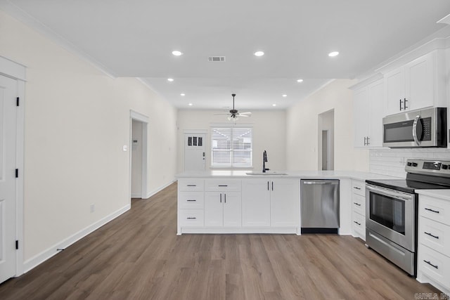 kitchen with kitchen peninsula, appliances with stainless steel finishes, white cabinets, and sink