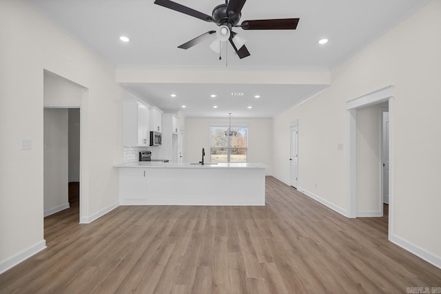 unfurnished living room featuring ceiling fan with notable chandelier, light wood-type flooring, and sink