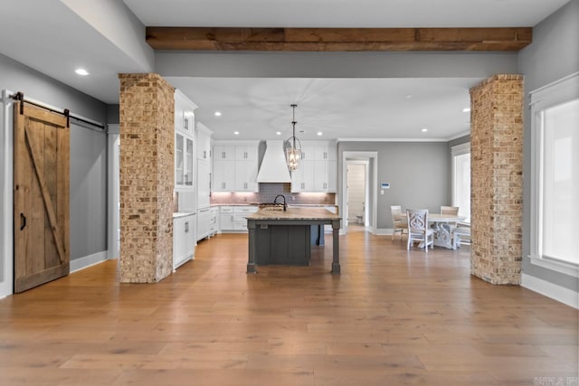 kitchen featuring pendant lighting, light hardwood / wood-style flooring, white cabinetry, and an island with sink