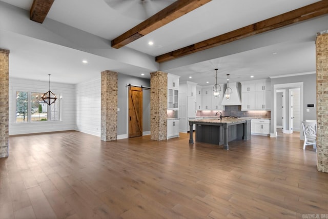 kitchen featuring a barn door, white cabinetry, a center island with sink, and hanging light fixtures