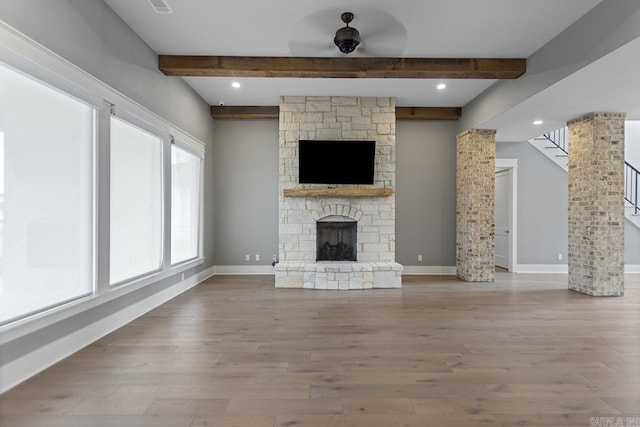 unfurnished living room with a stone fireplace, ceiling fan, hardwood / wood-style floors, and beamed ceiling