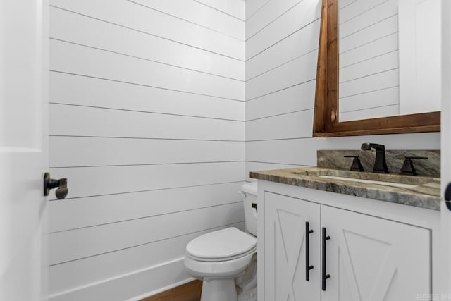 bathroom featuring vanity, toilet, and wooden walls