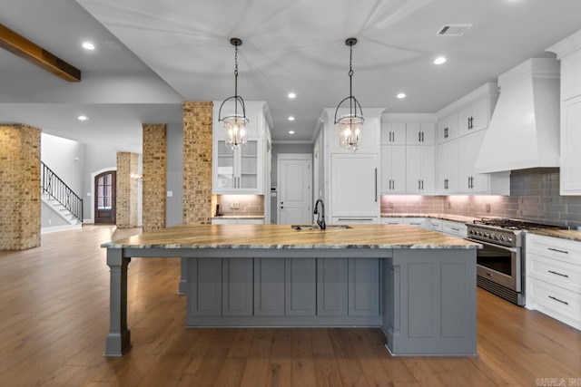 kitchen featuring hardwood / wood-style floors, custom exhaust hood, sink, stainless steel range, and a large island