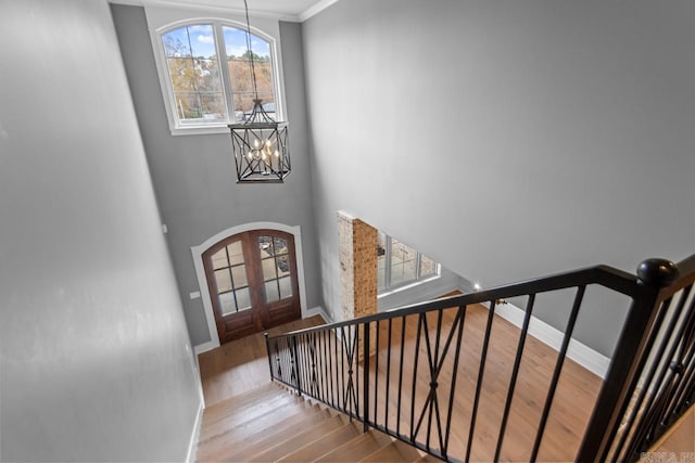 stairway featuring hardwood / wood-style floors, ornamental molding, french doors, and an inviting chandelier