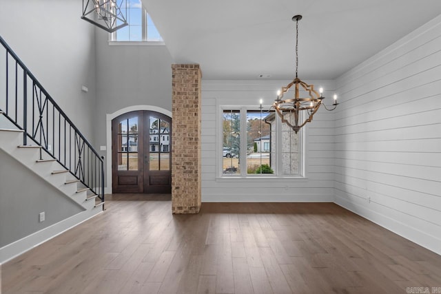 unfurnished dining area with french doors, a towering ceiling, dark wood-type flooring, an inviting chandelier, and wood walls