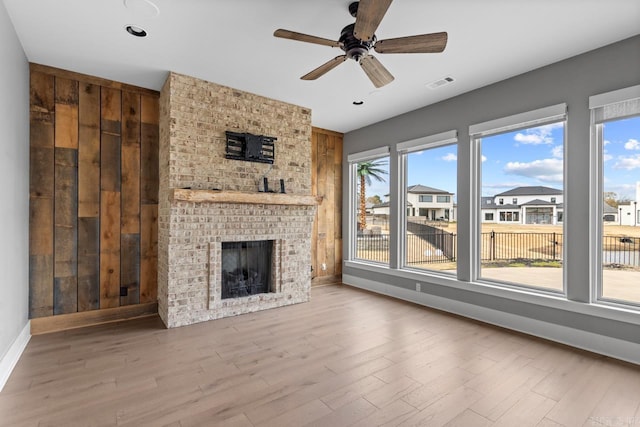 unfurnished living room featuring hardwood / wood-style flooring, plenty of natural light, wooden walls, and a brick fireplace