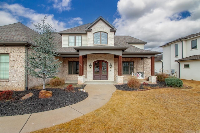 view of front facade featuring covered porch, a front yard, and french doors