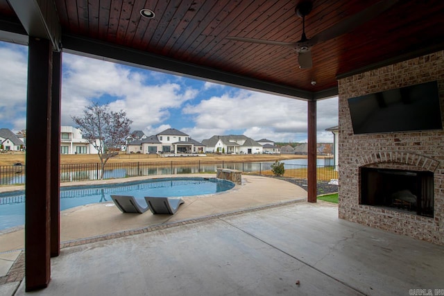 view of pool with a patio area, ceiling fan, a water view, and an outdoor brick fireplace