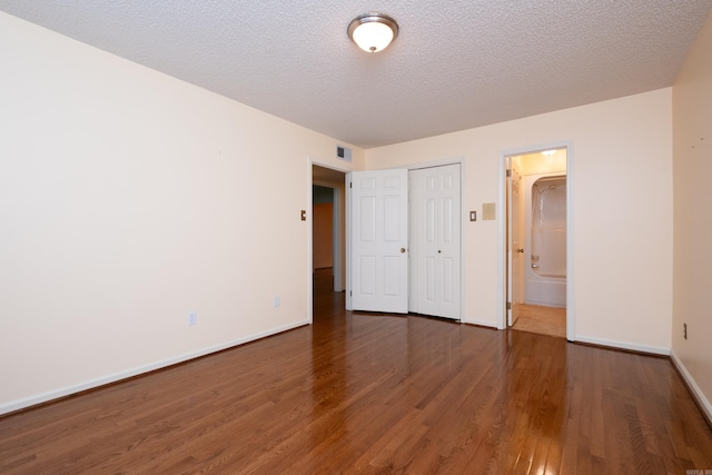 unfurnished bedroom featuring ensuite bathroom, a closet, dark wood-type flooring, and a textured ceiling