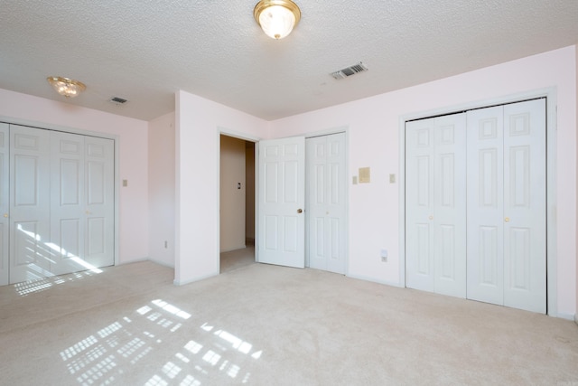 unfurnished bedroom with multiple closets, light carpet, and a textured ceiling